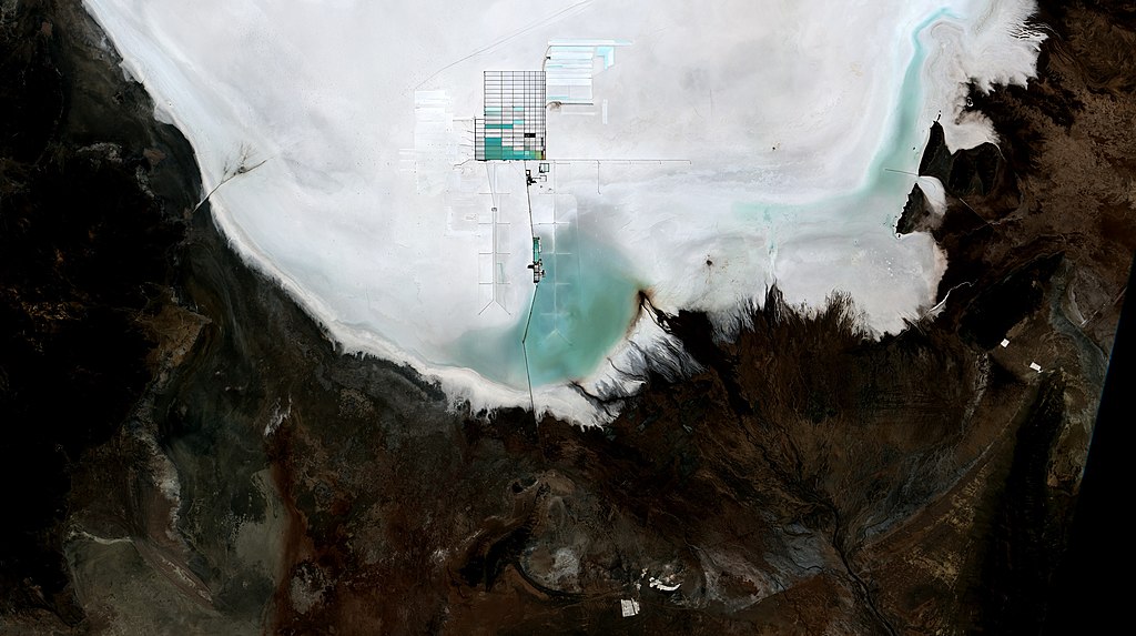 vista aérea del Salar de Uyuni en Bolivia: el salar es el área blanco, con terreno seco pero no salado a sus alrededores. En el centro del salar se ve una parte dividida en pequeños rectángulos que son los estanques de evaporación donde extraen el litio de los minerales del salar.