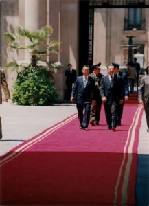 foto de Alberto Fujimori caminando en una alfombra roja al lado de otro hombre en traje civil y frente a otros dos hombres en uniformes militares