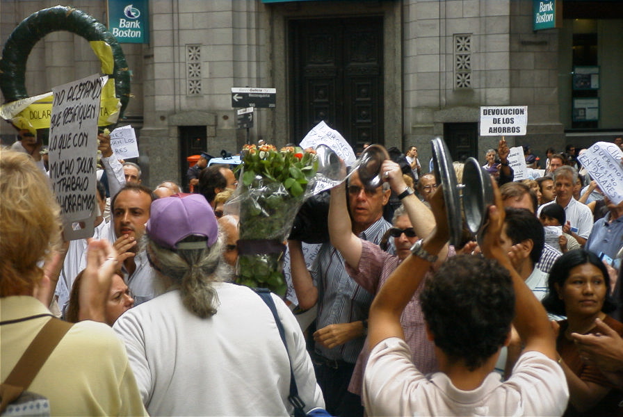 cacerolazo en Buenos Aires enfrente del edificio de Bank Boston; hay muchas personas juntas, varias que golpean ollas y cubiertos de ollas, y otros muchos que llevan pancartas que dicen cosas como "Devolución de los ahorros" y "No aceptamos que resaquen lo que con mucho dolor y trabajo ahorramos"